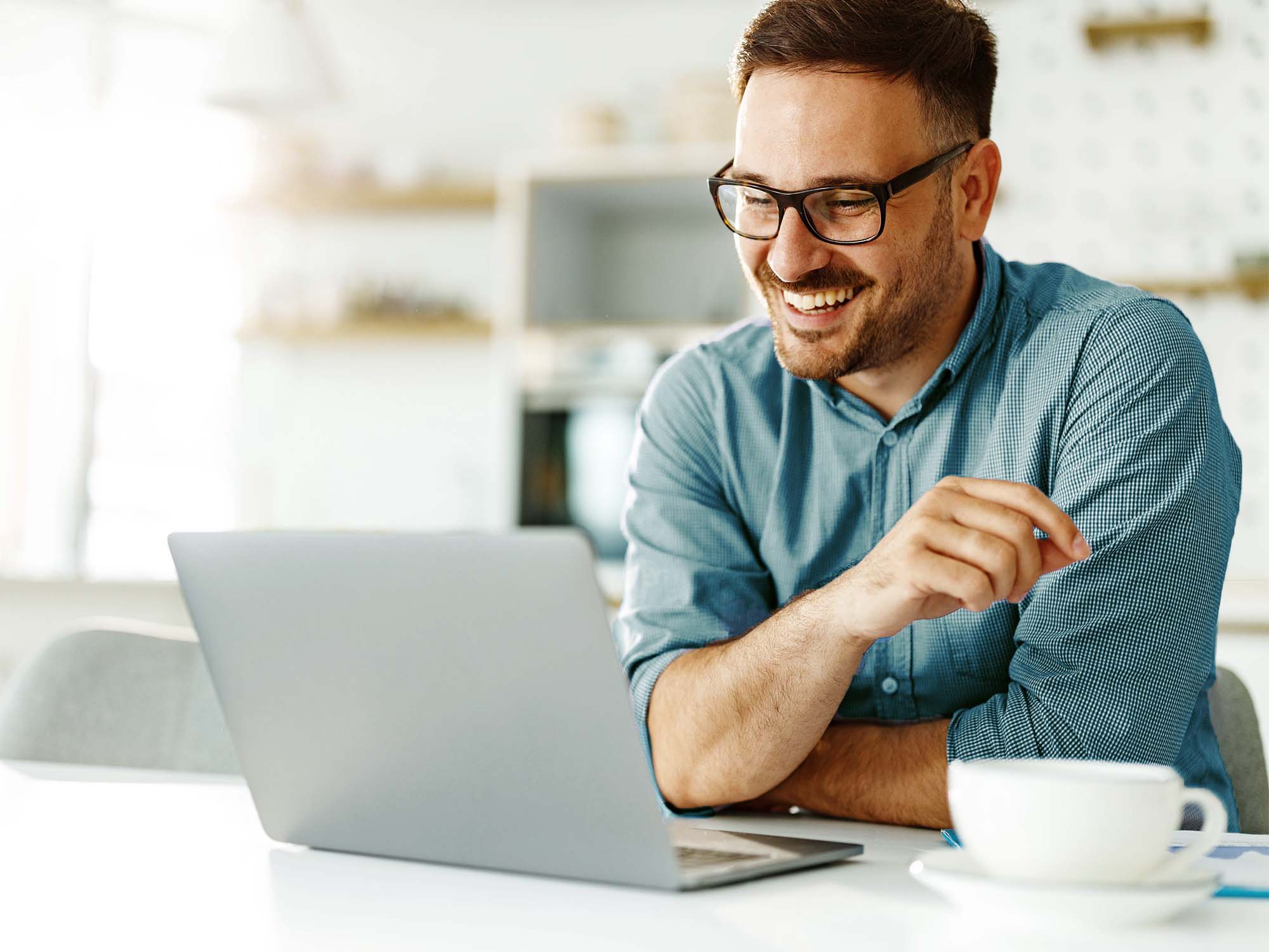 Mann im Wohnzimmer am Tisch, lächelt seinen Laptop an